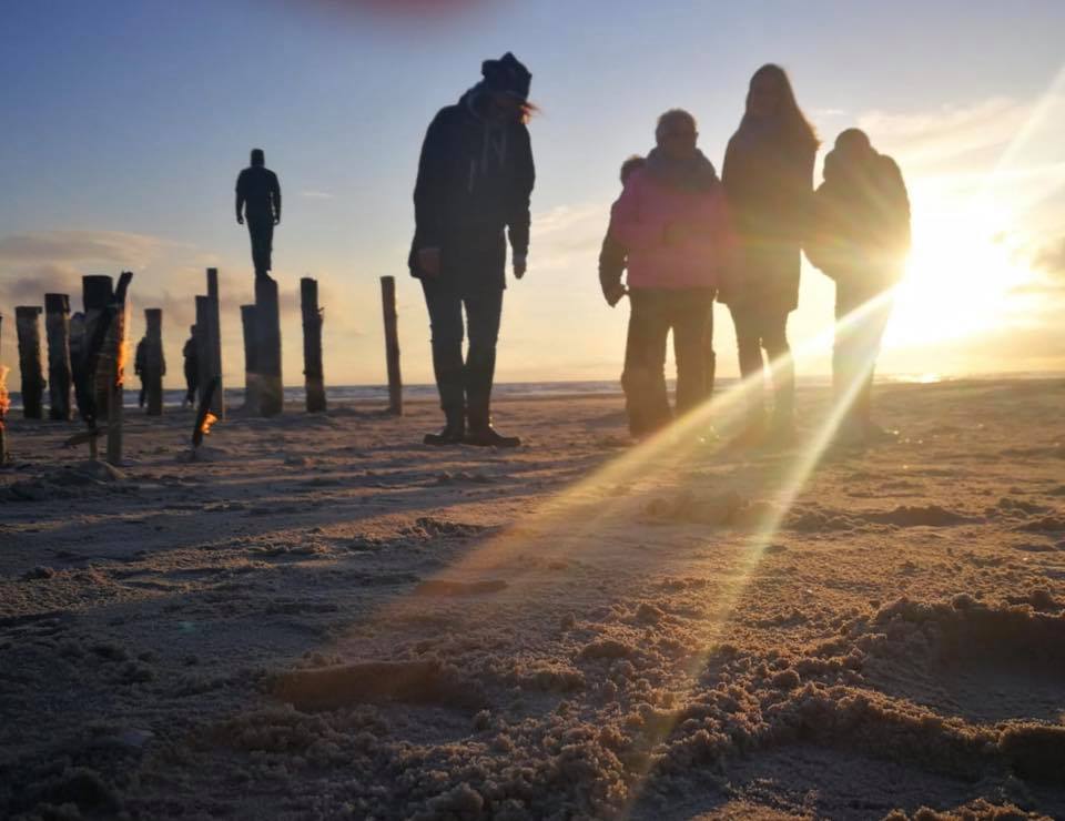 Eine Gruppe von Menschen steht bei Sonnenuntergang am Strand.