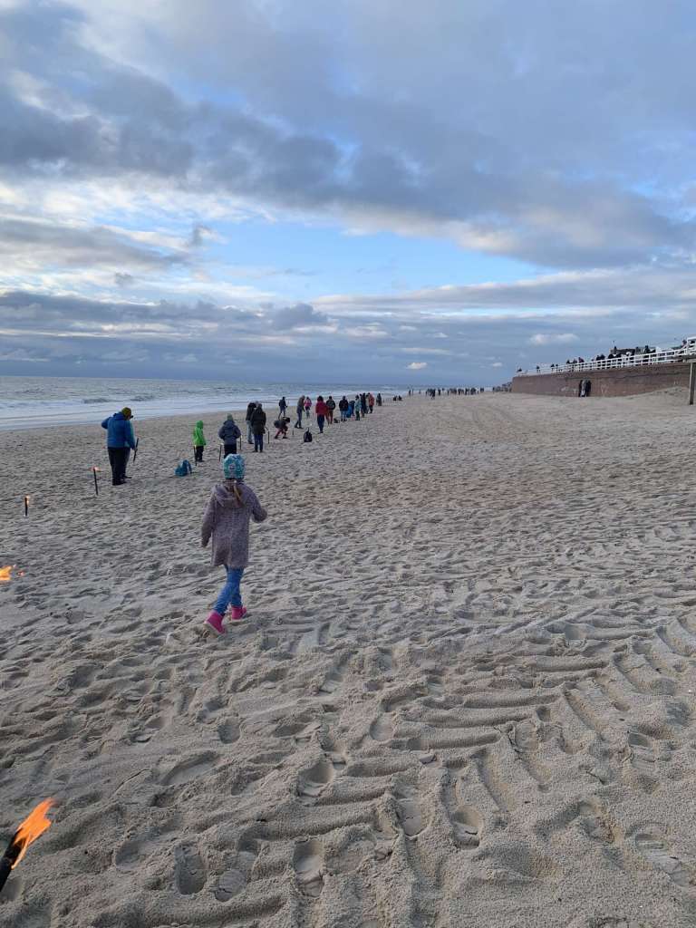 Eine Gruppe von Menschen, die mit Fackeln am Strand spazieren gehen.