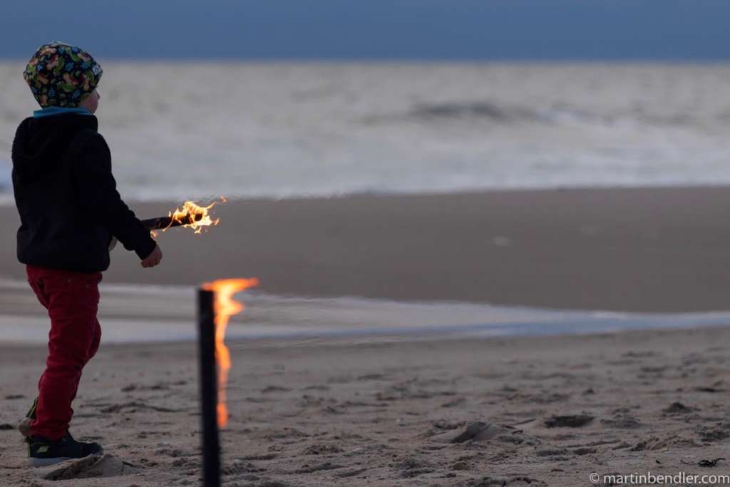Ein kleiner Junge hält eine Fackel am Strand.