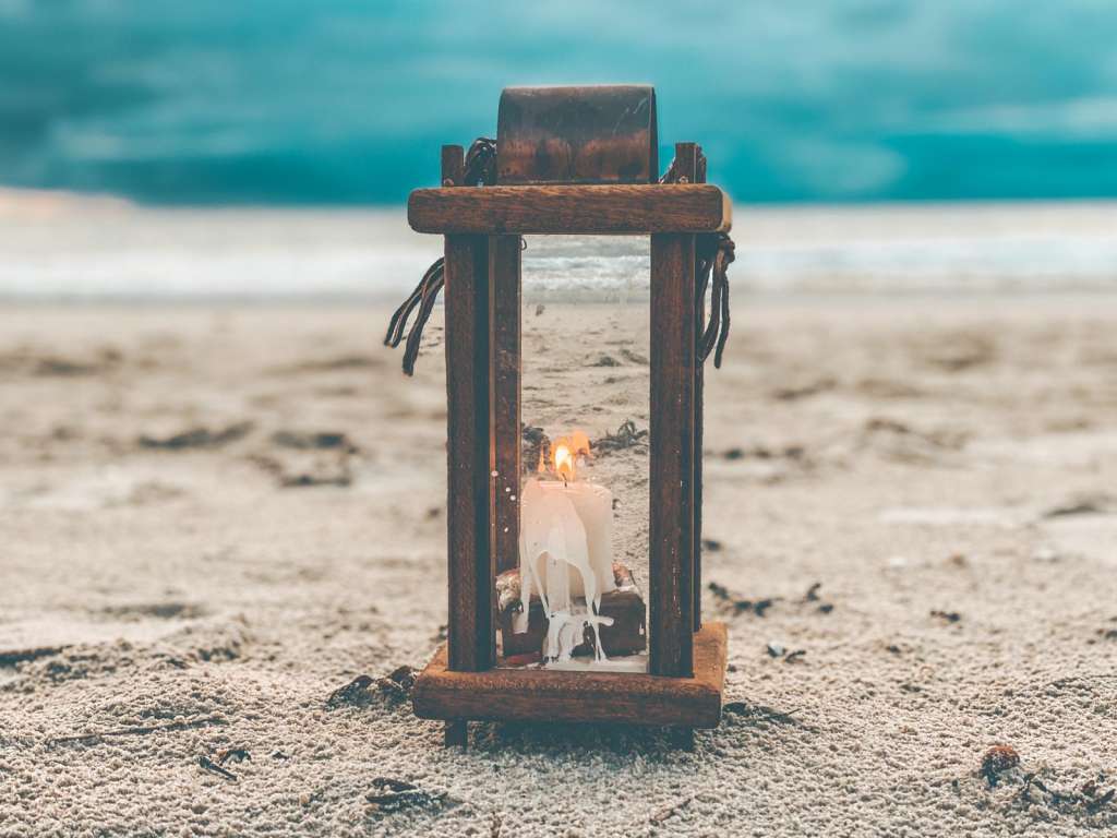 Eine hölzerne Laterne, die auf dem Sand neben dem Meer steht.